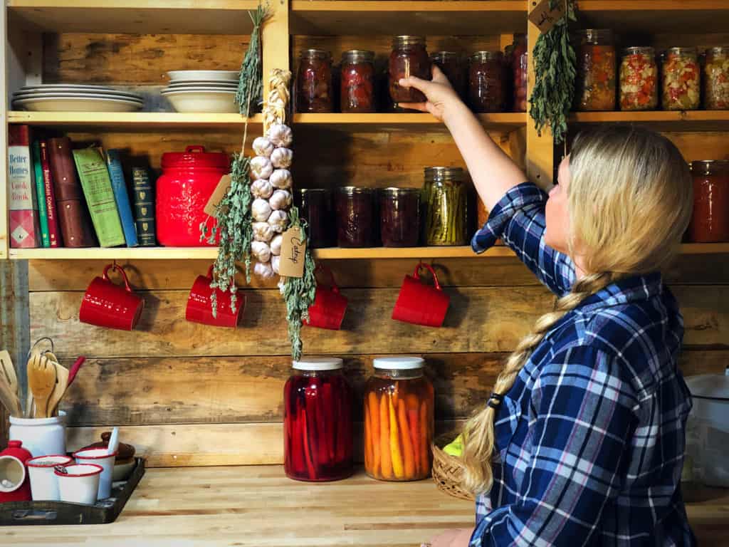 Woman reaching for a jar of food from a shelf up high.