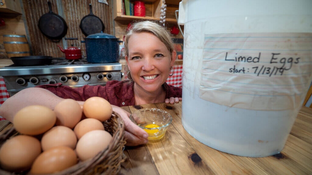 A woman behind a bucket with water glassed eggs, and a basket of fresh eggs.