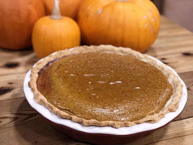 A pumpkin pie sitting on a table with fresh pumpkins in the background.