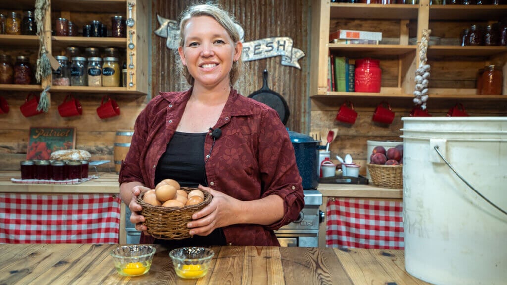 A woman holding a basket of eggs next to a bucket of water glassed eggs.