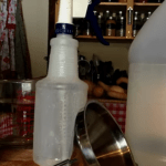 Bottle of dish soap, a plastic spray bottle and a large bottle of vinegar sitting on a counter.