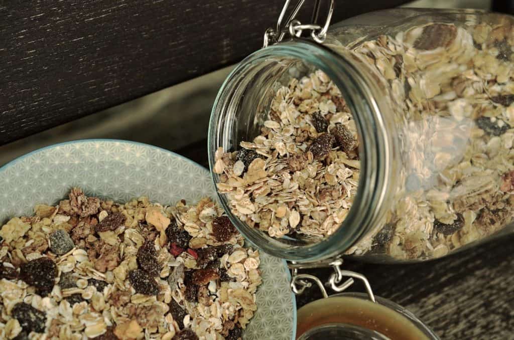 Large glass storage jar with muesli being poured into a bowl.