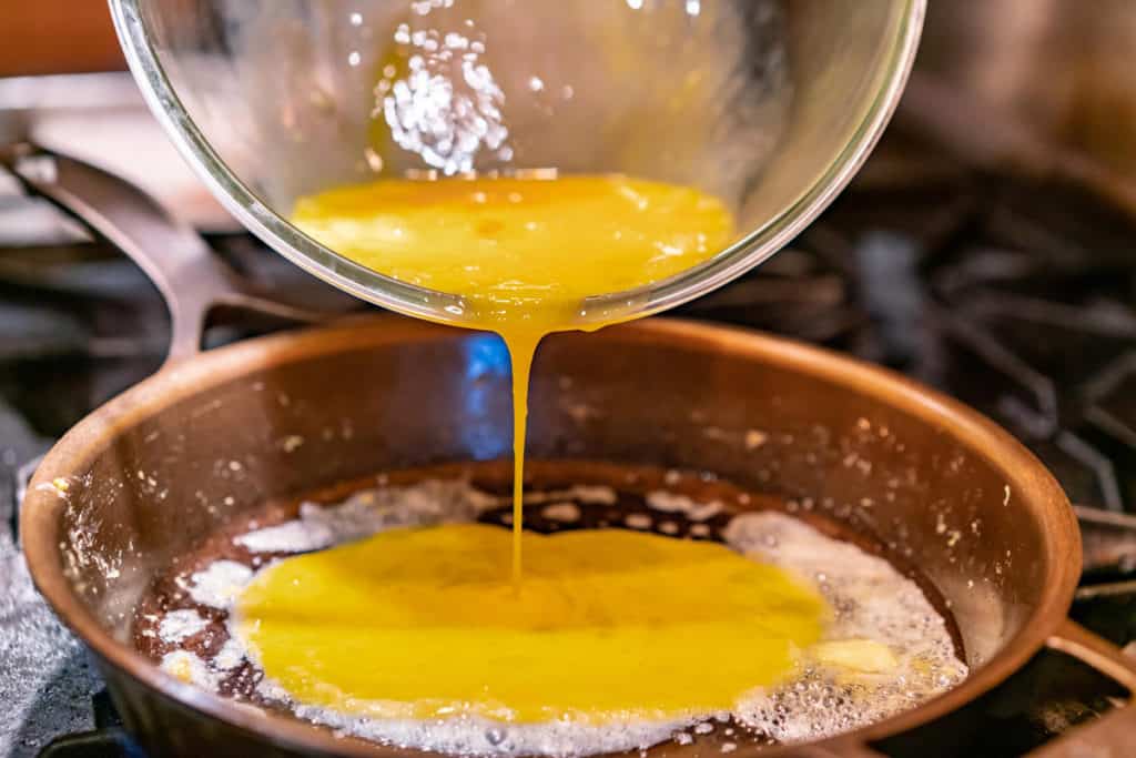 Uncooked scrambled eggs being poured into a buttered cast iron pan.