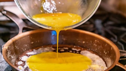Uncooked scrambled eggs being poured into a buttered cast iron pan.
