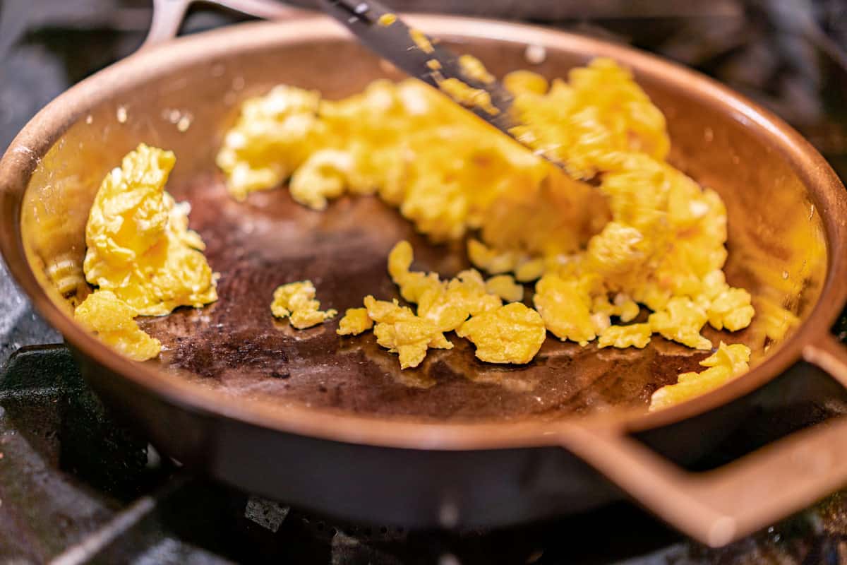 Scrambled eggs being cooked in a cast iron pan.