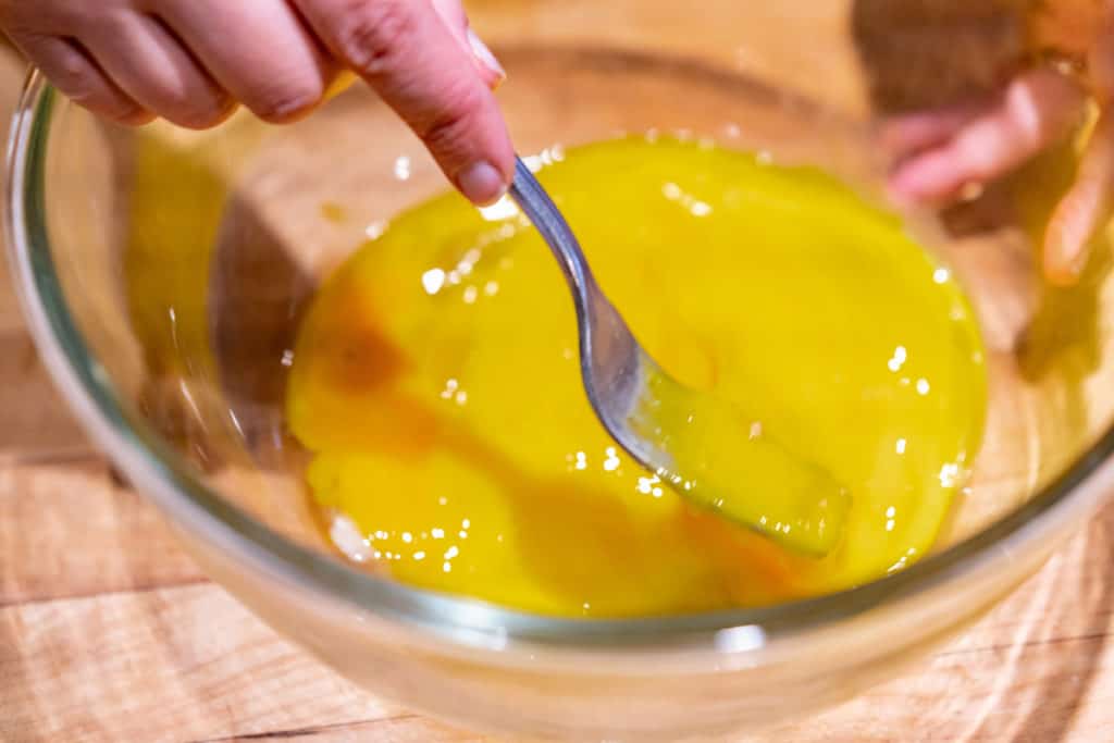 A clear glass bowl with eggs being scrambled with a fork.