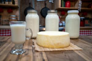 Three half gallon jars of raw milk and cream, a glass of raw milk and a large cheese wheel.