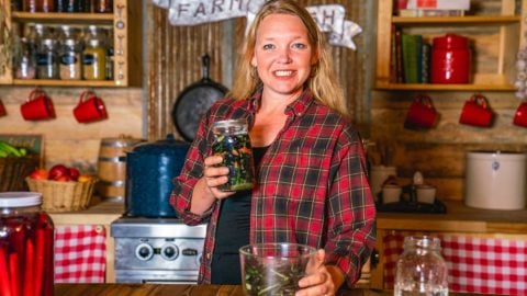 A woman holding up a jar of fermented green beans.