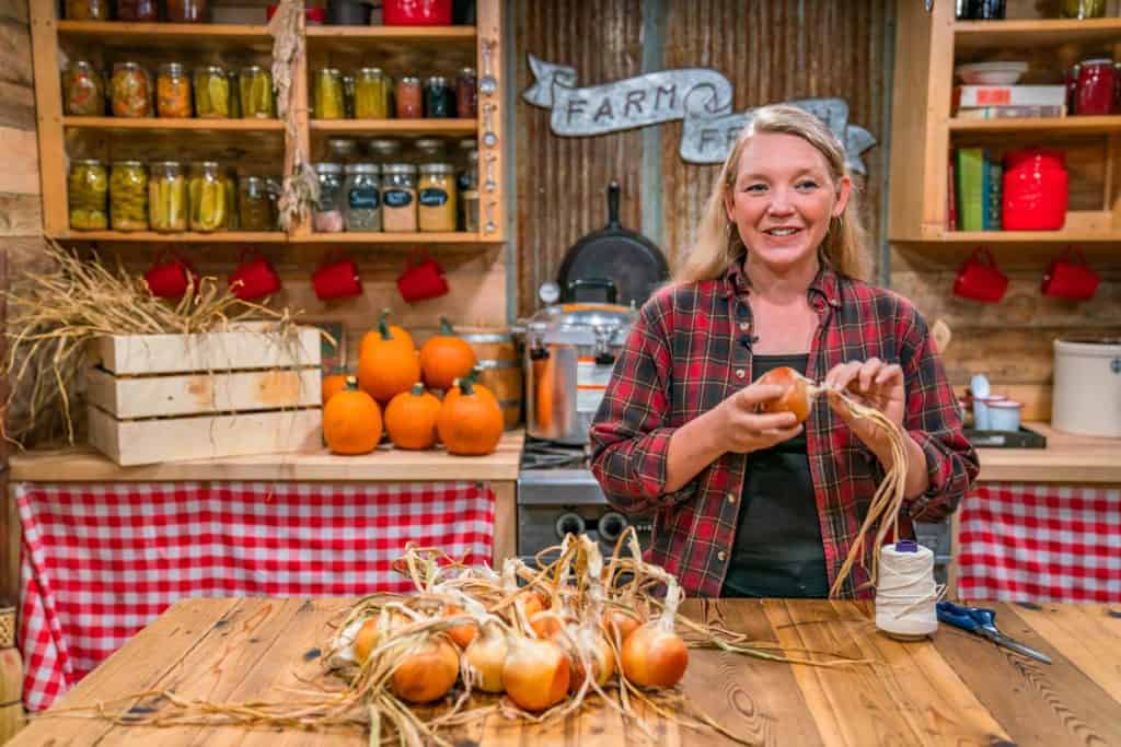 A woman holding an onion with the stem still attached.