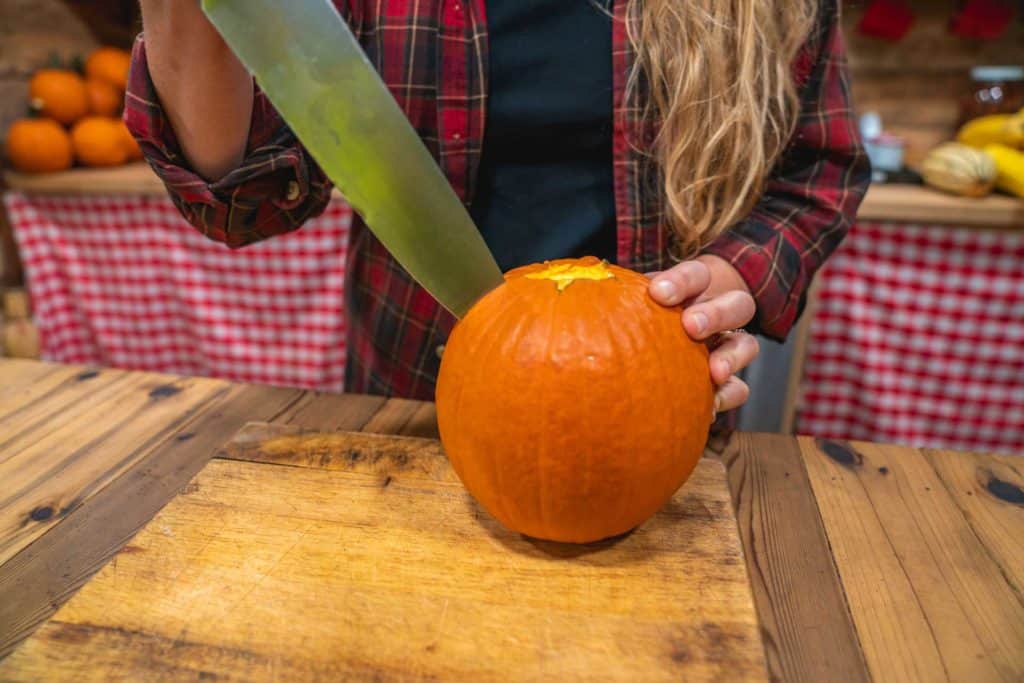 A woman piercing a pie pumpkin with a large knife.