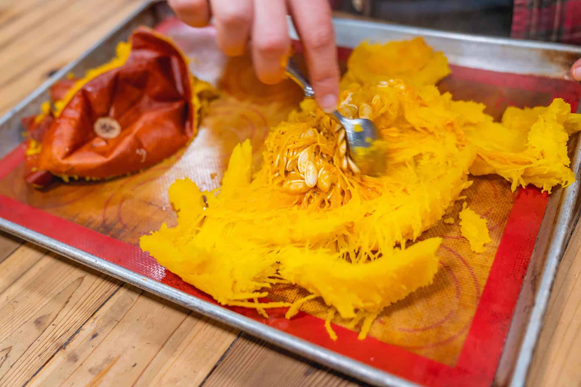 A fork scraping out the seeds from a roasted and peeled pie pumpkin.