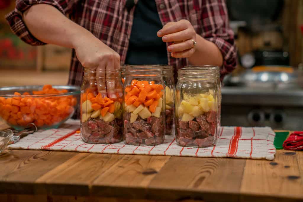 A woman packing in raw carrots into canning jars.