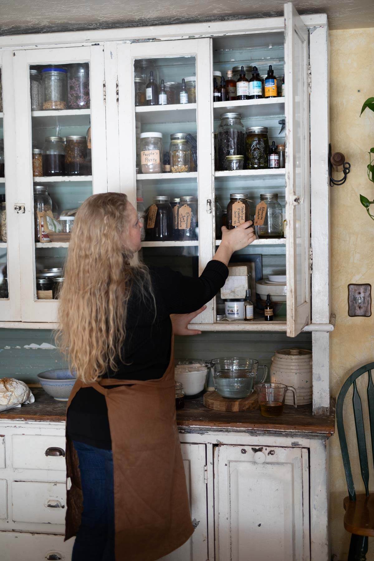 A woman adding medicinal herbs into a kitchen cabinet.
