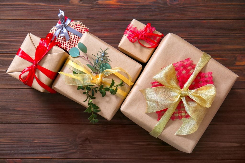 Five gift boxes wrapped for Christmas with bows and greenery.