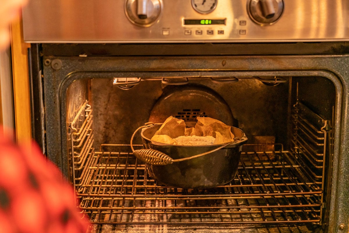 Cast iron dutch oven in the oven with a loaf of artisan bread inside.