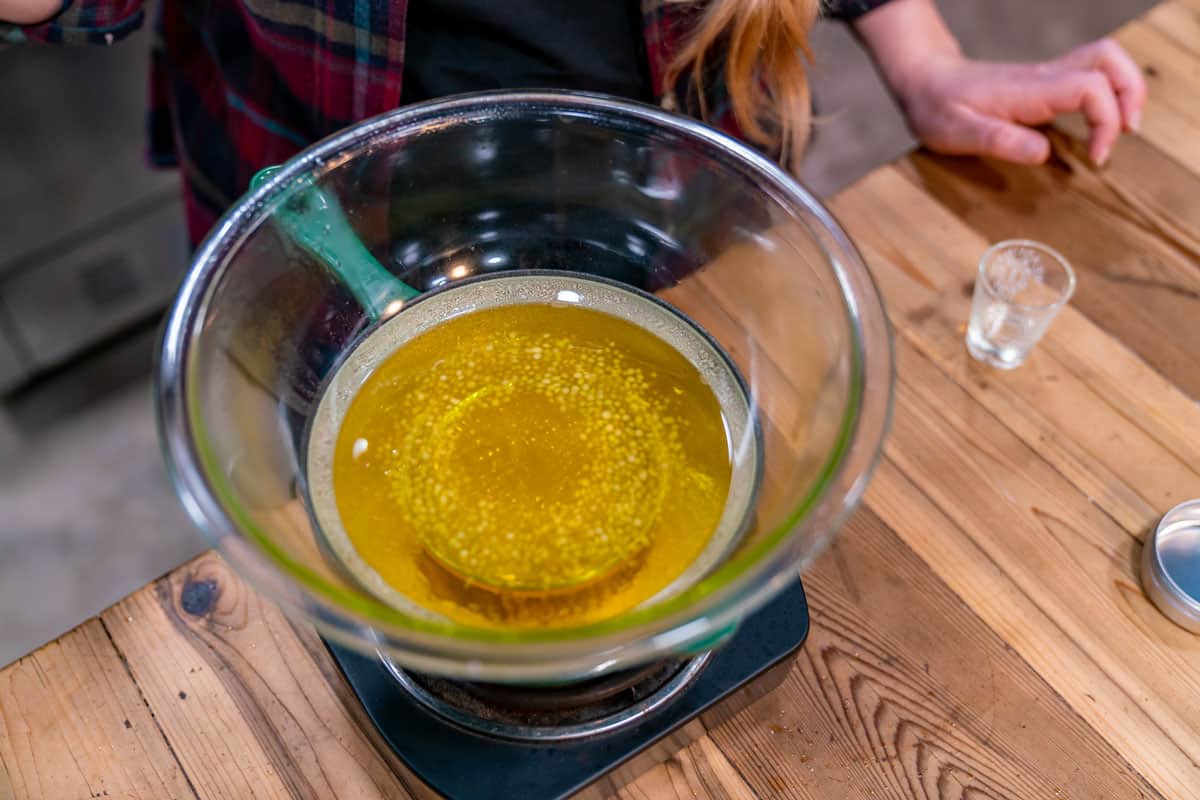 A large glass bowl with oil and beeswax pellets over a double boiler.