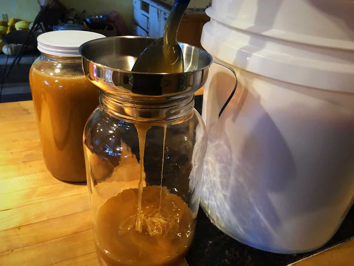 Honey being ladled from a five gallon container into a one gallon jar.