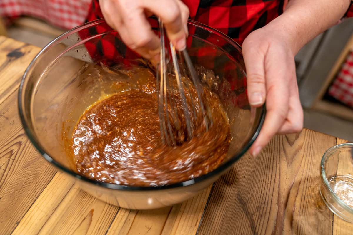 A whisk mixing sourdough brownie batter in a glass bowl.