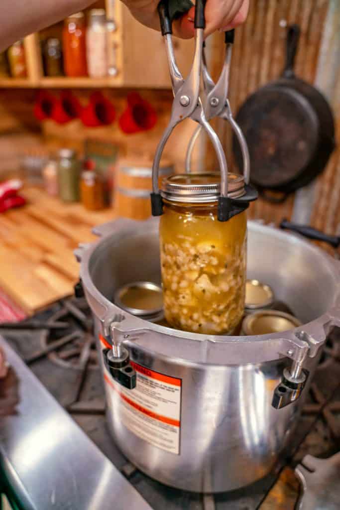 A jar of home canned chicken chili being lifted out of the pressure cooker.