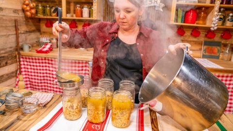 A woman ladling chicken chili into mason jars.