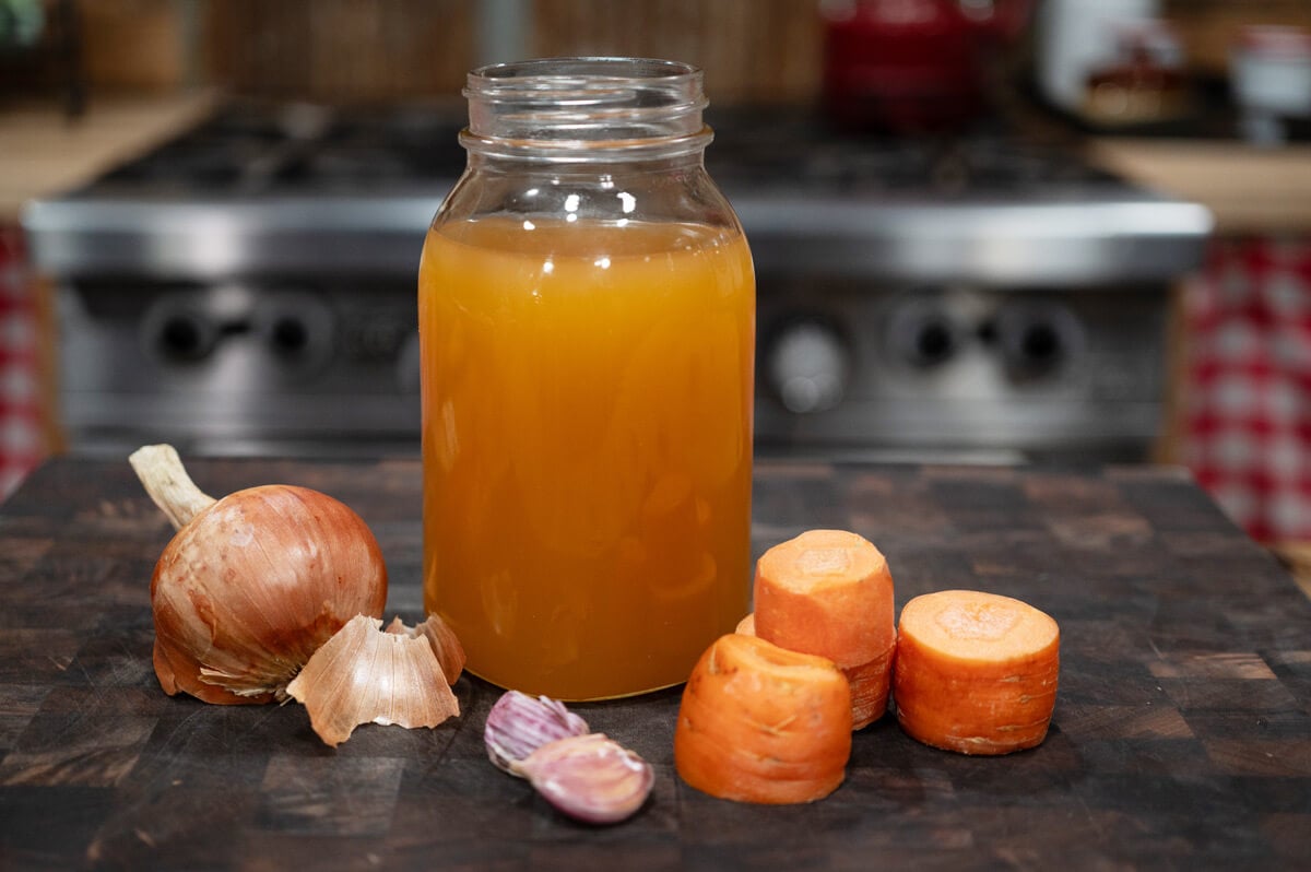 A jar of homemade chicken bone broth surrounded by chopped vegetables.