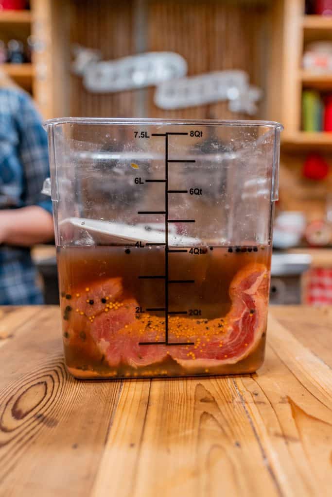 A beef brisket inside a food-grade bucket soaking in a brining liquid.