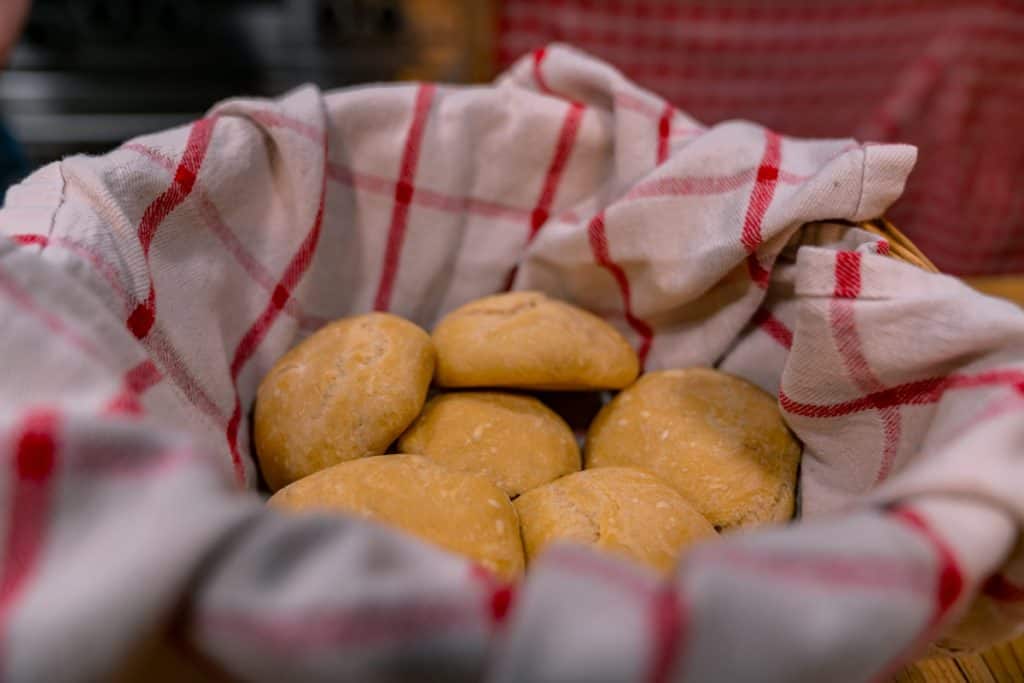 A basket with a red and white checkered towel filled with rolls.