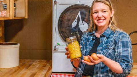 A woman standing in front of a harvest right freeze dryer holding a jar of powdered eggs in one hand and farm fresh eggs in the other hand.