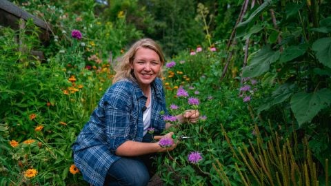 A woman kneeling in a cottage garden next to flowers.