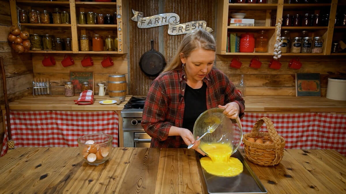 A woman pouring whisked eggs from a bowl onto a freeze drying tray.