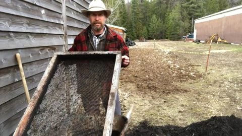 A man holding up one side of a compost sifter.
