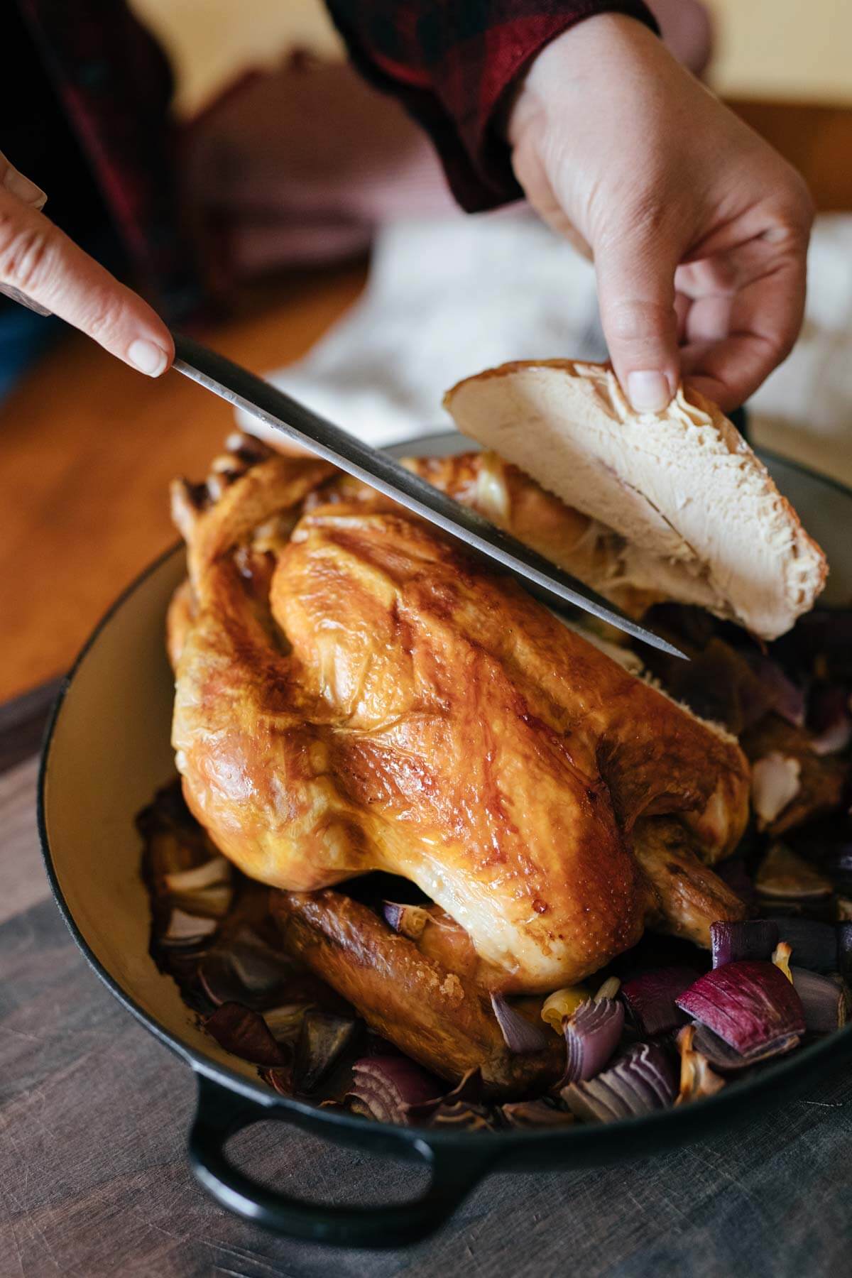 Hands carving a whole roasted chicken.