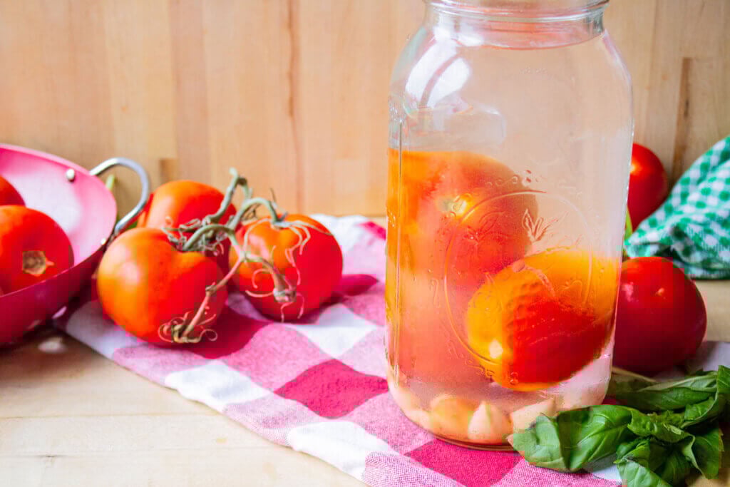Whole fermented tomatoes in a glass Mason jar.