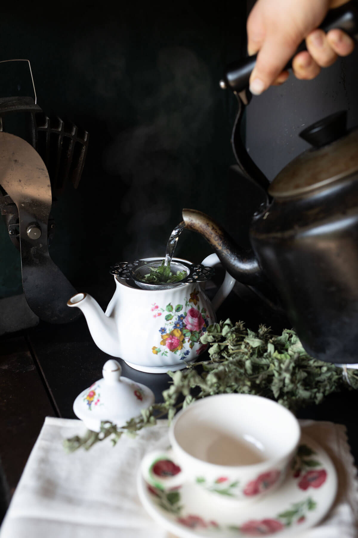 A teakettle pouring water into a strainer full of herbs.
