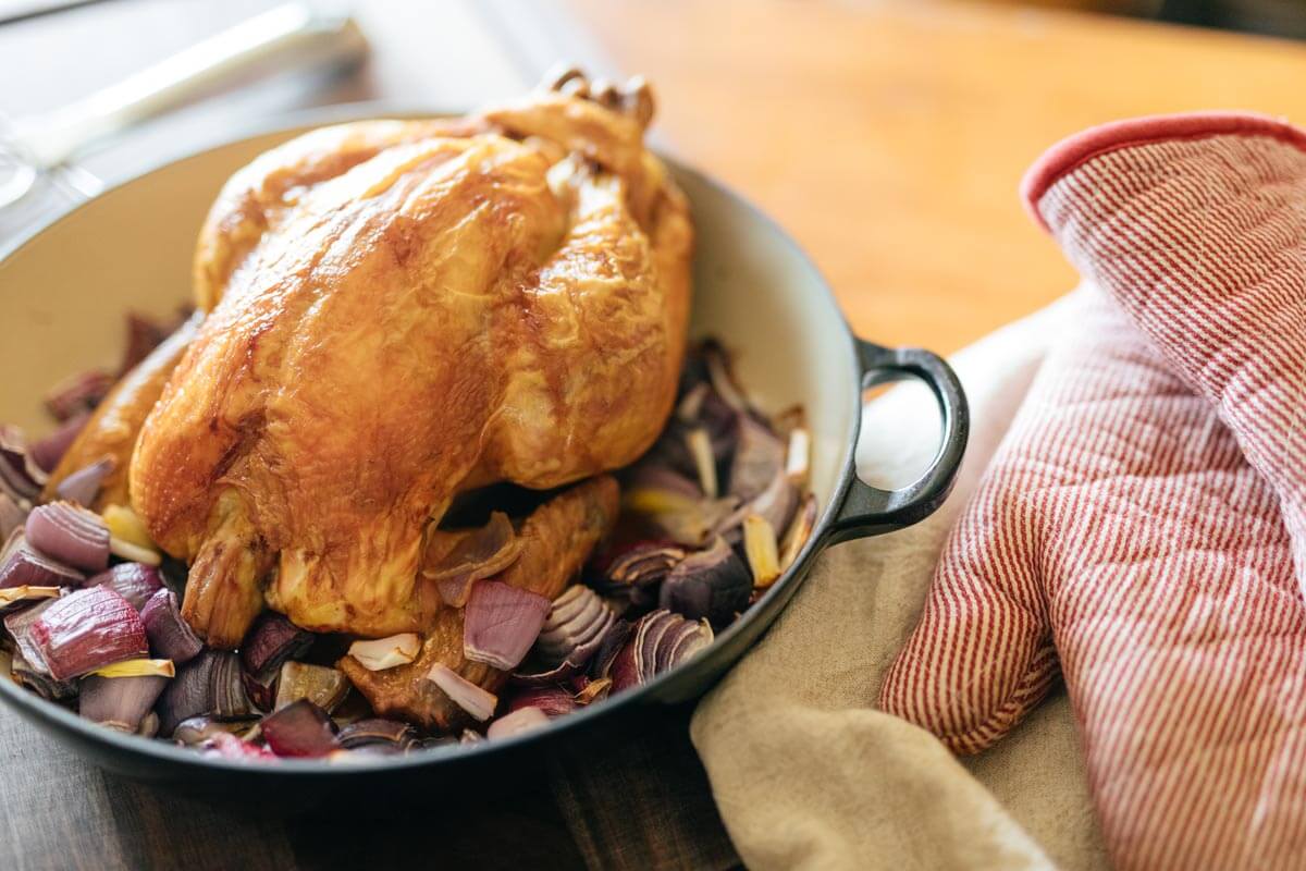 A whole roasted chicken sitting in a Dutch oven on top of vegetables.
