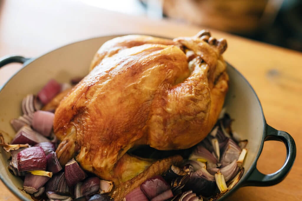 A whole roasted chicken sitting in a Dutch oven on top of vegetables.
