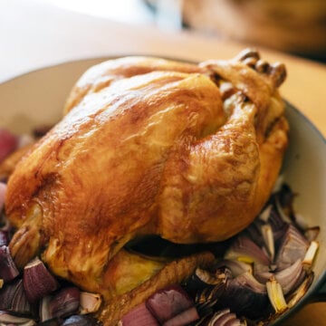 A whole roasted chicken sitting in a Dutch oven on top of vegetables.
