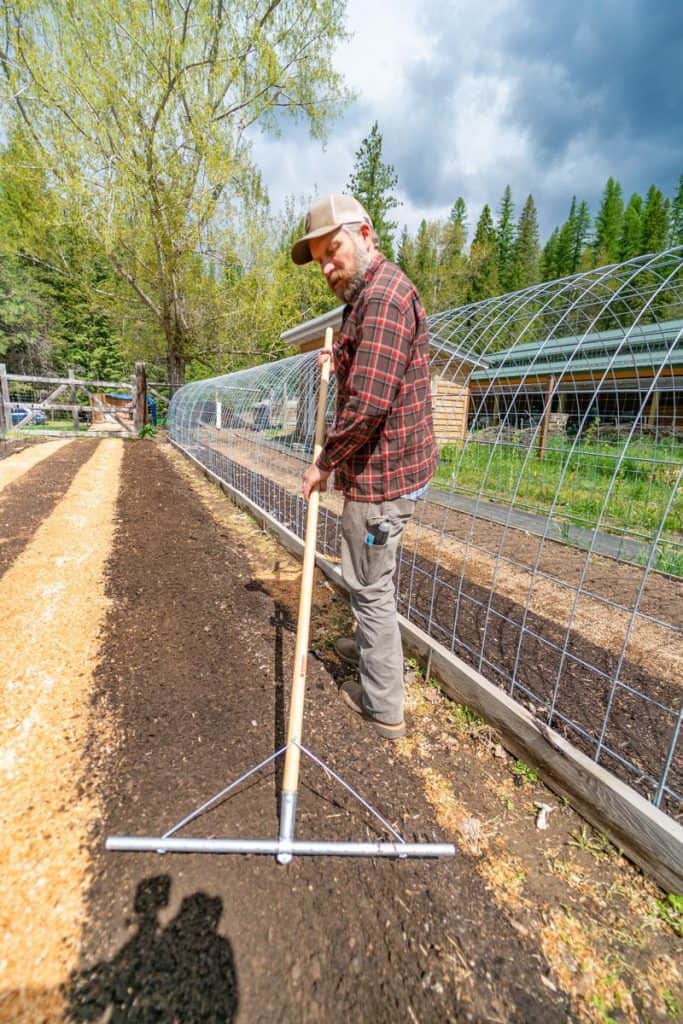 A man raking a long garden bed row to smooth the soil.