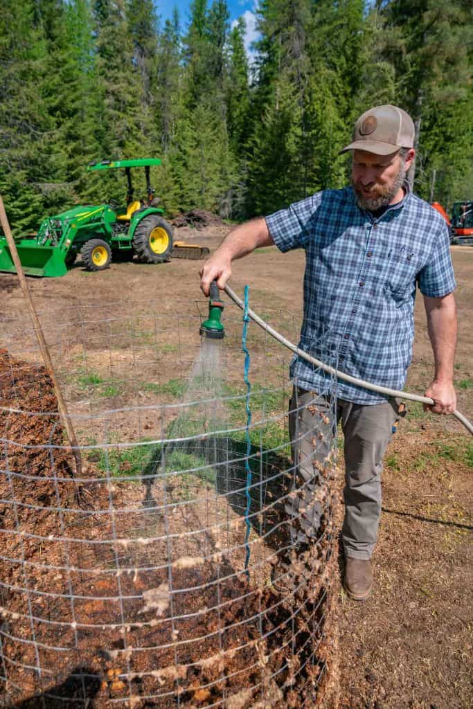 A man spraying a compost pile with a hose.