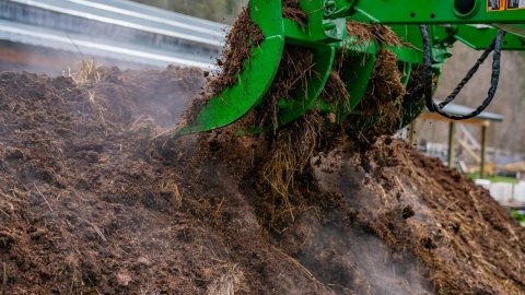 A large tractor turning a compost pile.