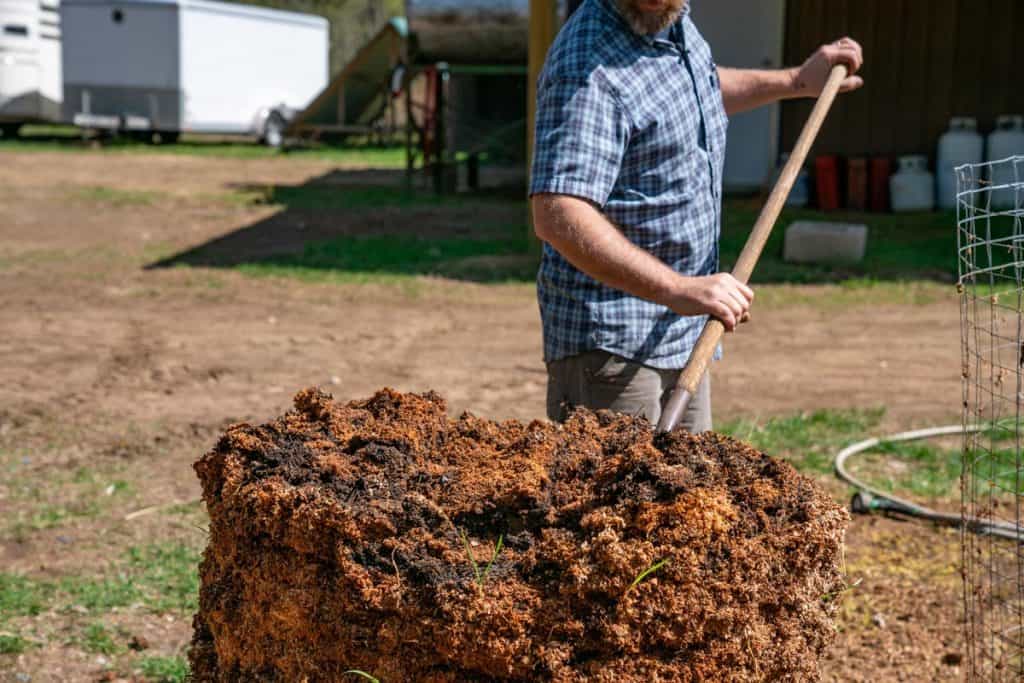 A man scooping compost with a pitchfork.