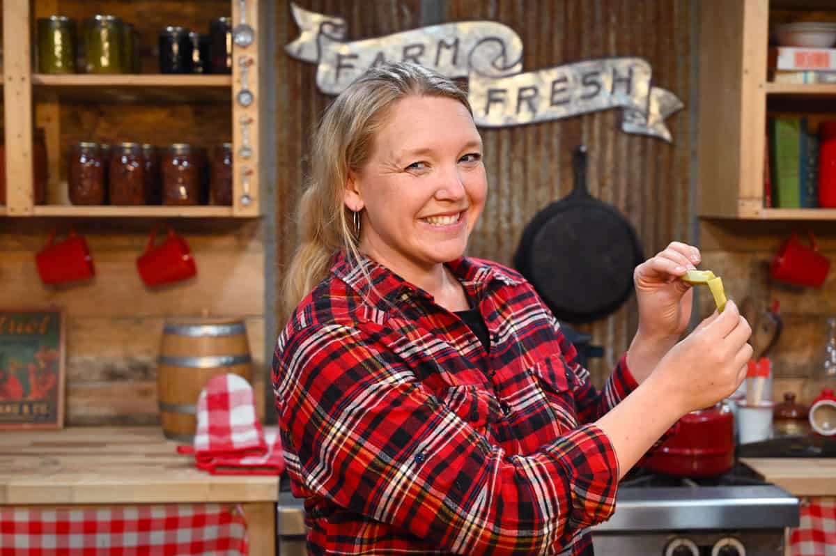 A woman holding up a pickle spear showing how crunchy they are by folding it in half.
