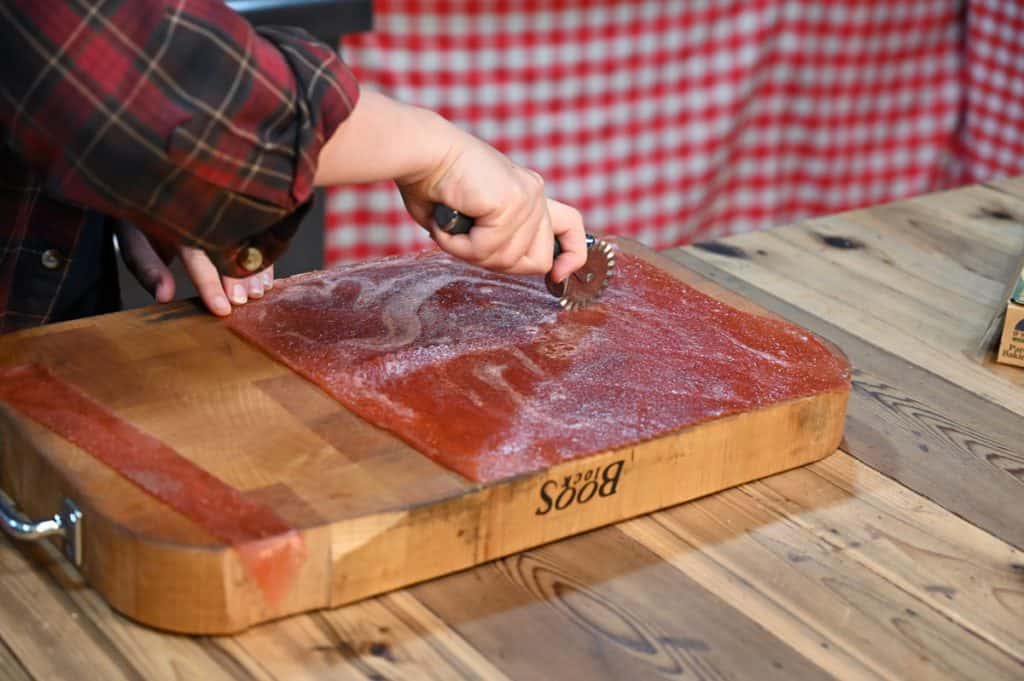 A woman's hands using a pastry cutter to cut a piece of fruit leather.