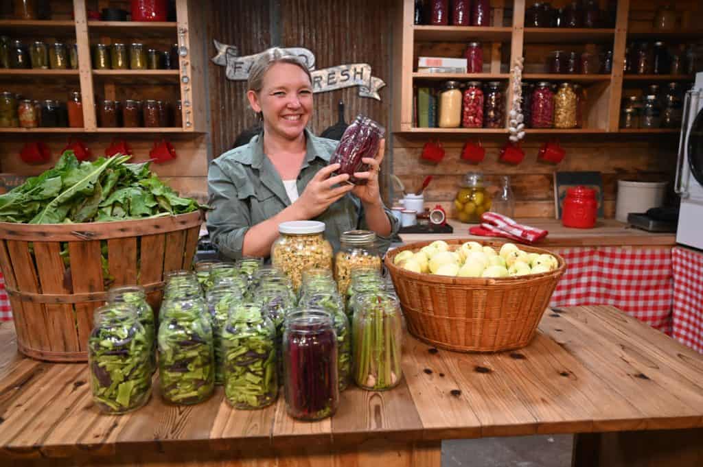 A woman standing behind a counter full of produce waiting to be preserved.