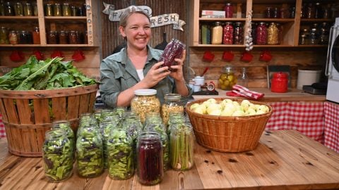 A woman standing behind a counter full of produce waiting to be preserved.