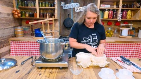A woman pressing fresh cheese into a cheese mold.