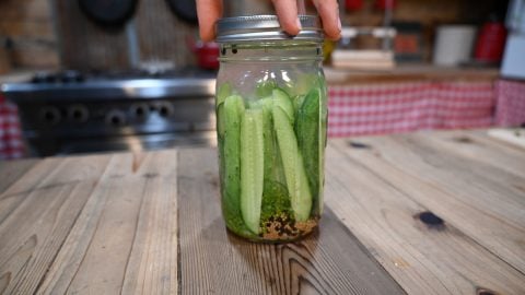 A hand screwing a lid onto a mason jar filled with pickle spears.