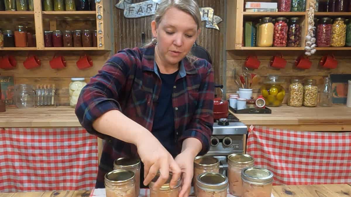A woman tightening the band on a jar of chicken ready to be canned.