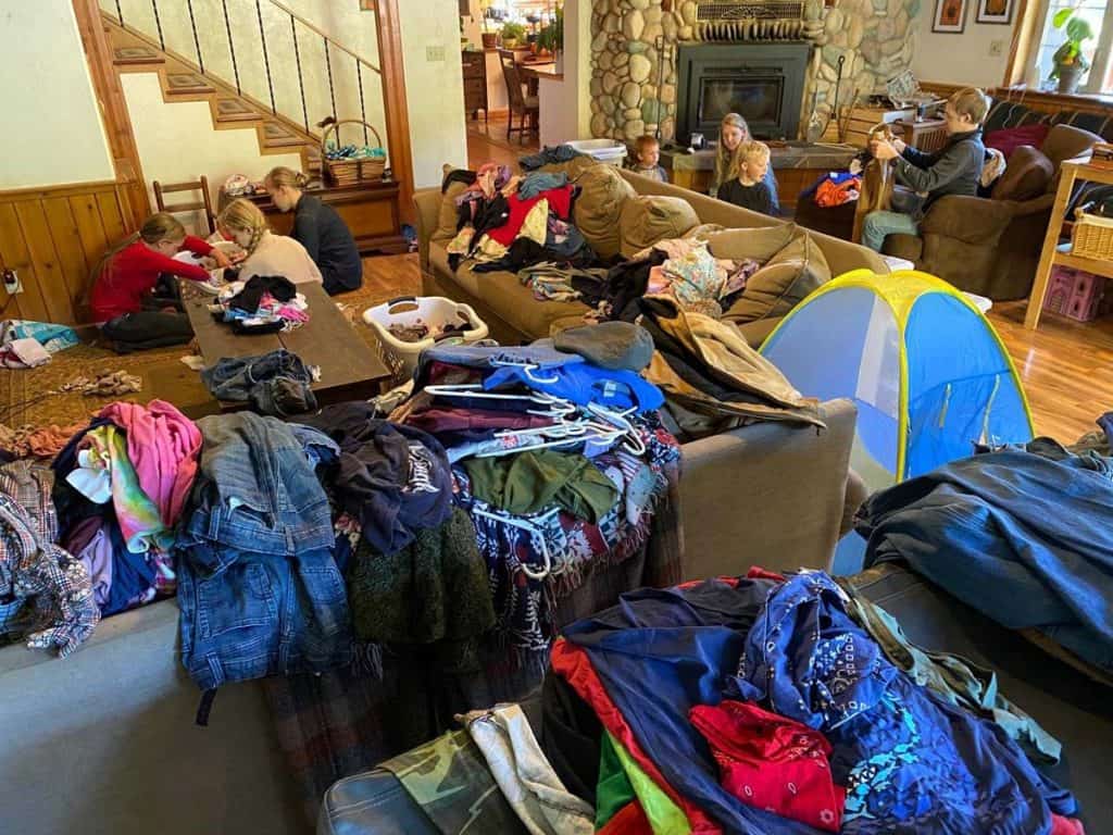 Clothes piled all over a living room with kids and a mom looking through them.