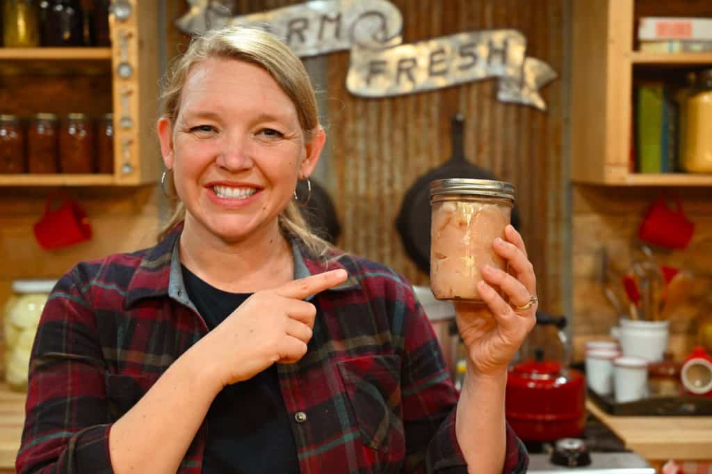 A woman holding up a jar of home-canned chicken.